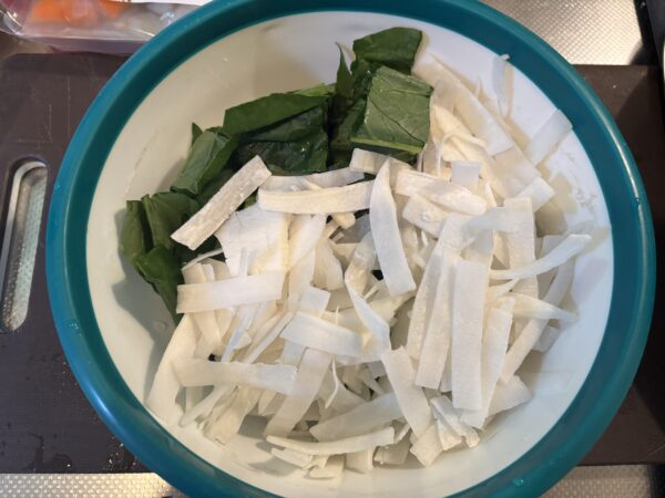 ボウルにカットした小松菜と大根を入れ、加熱準備をする様子