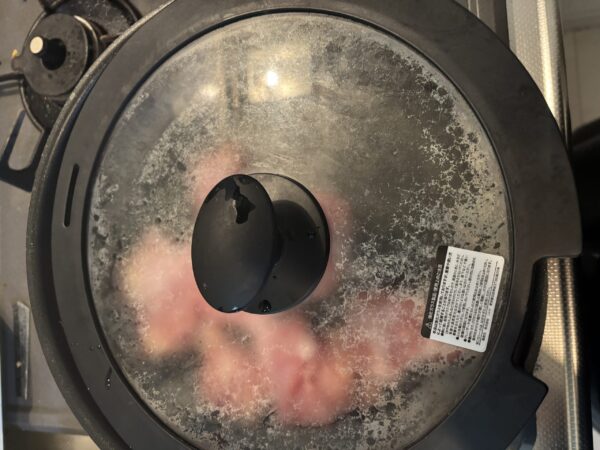 フライパンに蓋をして鶏肉をじっくりと蒸し焼きにしている様子