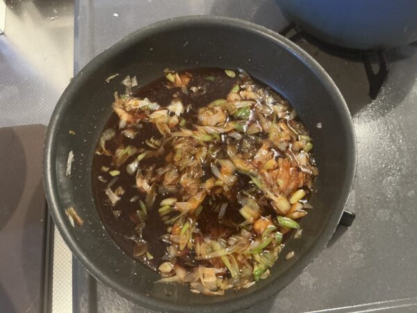 炒めた長ネギに特製だれを加え、強火で煮詰めてタレを完成させる様子