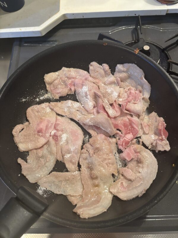 豚肉にごま油と片栗粉をまぶし、フライパンで両面を焼き付ける様子