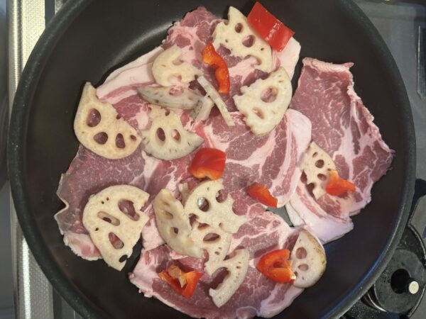 パプリカをキッチンバサミでカットし、レンコンなどの具材と一緒に炒める様子