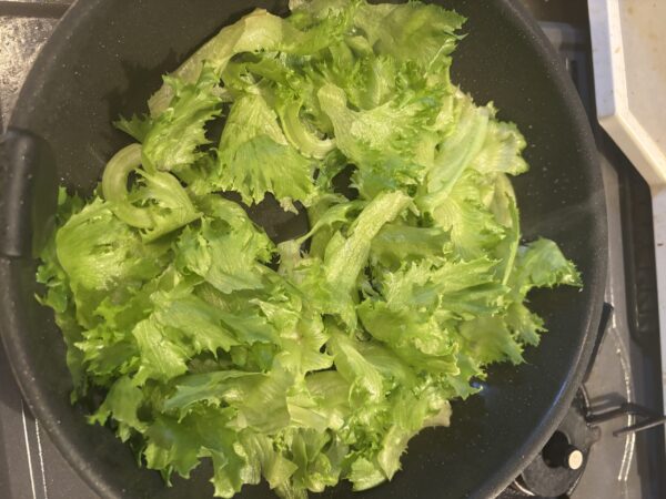 強火で熱したフライパンにちぎったレタスを入れ、サッと油通しする工程