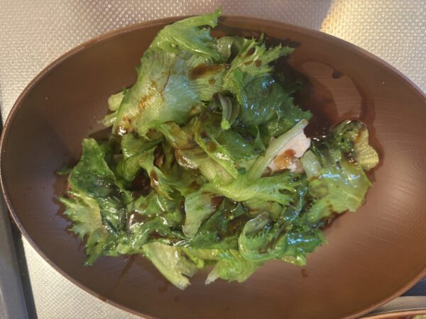 器に盛った具材に仕上げのオイスターソースを回しかけて主菜を完成させる様子