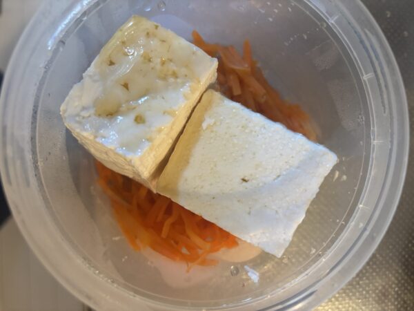 加熱したにんじんに豆腐、塩、ごま油を加えて混ぜ、小ネギを散らして副菜を仕上げる様子